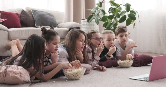 Children lying on floor watching movie and eating popcorn
