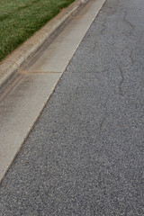 Asphalt residential street with formed concrete curb and green grass, vertical aspect
