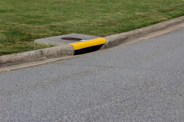 Residential street curb with drain painted yellow, green grass and asphalt copy space, horizontal aspect - obrazy, fototapety, plakaty
