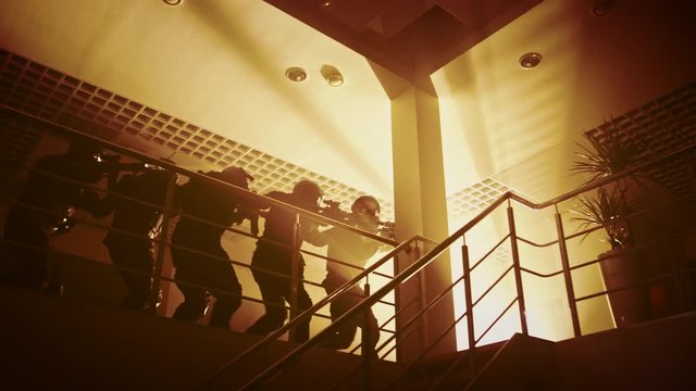 Masked Squad of Armed SWAT Police Officers Move in Formation on a Second Floor in an Office Building. Soldiers with Rifles and Flashlights Move Forwards and Cover Surroundings. Warm Color Grading.