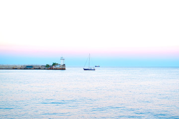 Obraz premium Sea sunset in summer in the evening with natural light Sea sunset, yachts in the sea near the lighthouse on a summer day in the background of beautiful colors in the sky 