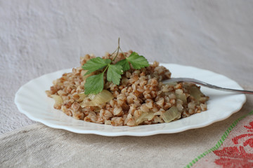 Fried buckwheat porridge with onions on a white plate on a grey background, side view, copy space