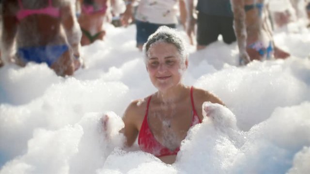 4k video of smiling and laughing young women covered in soap foam dancing on the beach party at bright sunny day