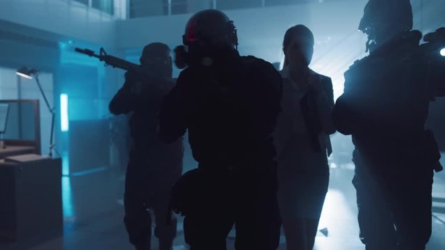 Masked Squad of Armed SWAT Police Officers Rescue a Female Hostage in a Dark Seized Office Building with Desks and Computers. Soldiers with Rifles and Flashlights Move Forwards and Cover Surroundings.