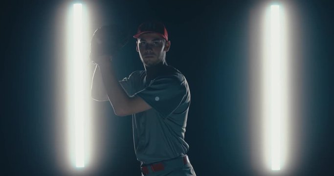 Caucasian professional baseball player pitcher throwing a ball towards camera against dark background. 4K UHD 60 FPS SLOW MOTION