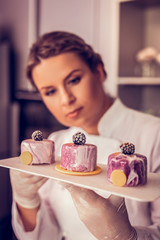 Positive delighted brunette woman examining colorful cakes