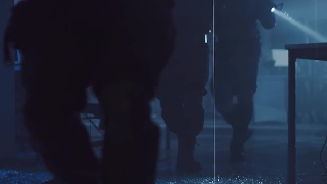 Close Up View of Masked Squad of Armed SWAT Police Officers Storm a Dark Seized Office Building with Desks and Computers. Soldiers with Rifles Walk on Broken Glass and Cover Surroundings.