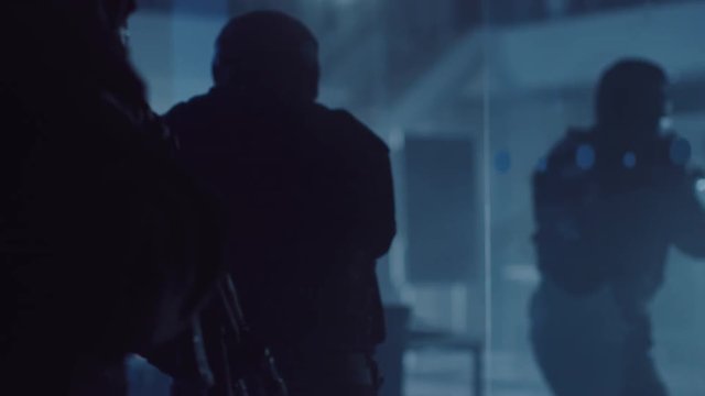 Close Up View of Masked Squad of Armed SWAT Police Officers Move Slowly in a Dark Seized Office Building with Desks and Computers. Soldiers with Rifles Walk on Broken Glass and Cover Surroundings.
