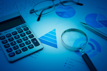 Magnifying glass, calculator, pen, and glasses on business budget graph, Financial research concept, blue tone