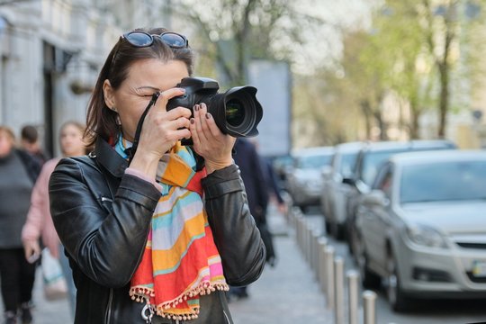 Mature woman with photo camera photographing on the street of spring city, female professional photographer,copy space