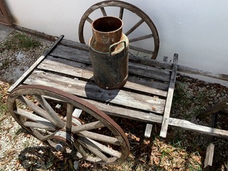 Carretilla antigua en madera para transportar mercancías y recipiente lechero de metal.