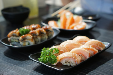 Set of Japanese food consist of Salmon sushi, Steamed rice topped with grilled eel (Unagi roll) and Fresh salmon sashimi on wooden table.