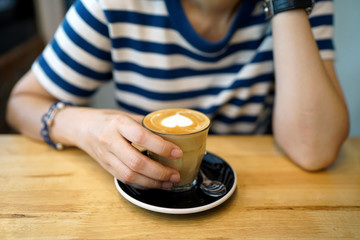 Hot Latte - Holding a cup of coffee with milk and beautiful heart pattern latte art on wooden table background, Perfect for breakfast time.