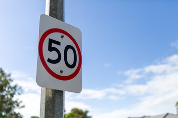 A speed limit sign marking a 50 kmph zone attached to a post with a cloudy blue sky behind.