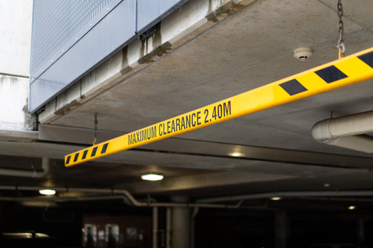 Suspended height restriction bar with hanger assemblies and chains over the entrance to a basement car park marks height limit of 2.40 metres.