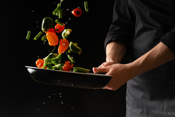 Cook prepares vegetables on a black background, oriental cuisine, tasty and healthy food, recipe book, menu, cooking