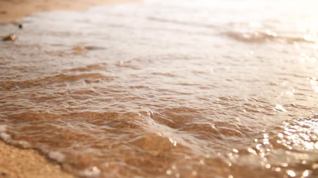 4k closeup video of sea waves wahing off footprints on the golden sand at beach