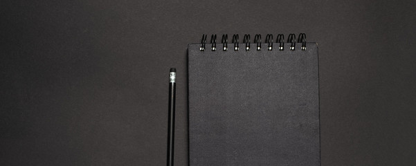 Top view of dark desk with black pencil and notebook. Mockup concept.