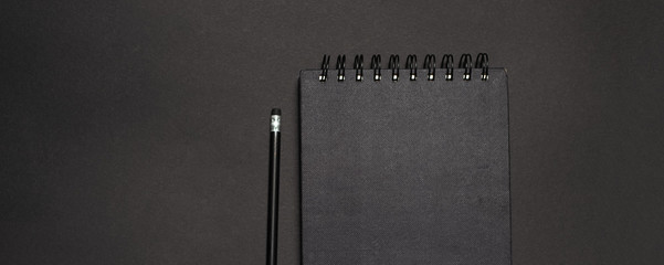 Top view of dark desk with black pencil and notebook. Mockup concept.