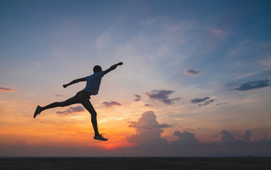 Happy man jumping for joy on the peak of the mountain, cliff at sunset. Success, winner, happiness