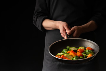 Chef preparing vegetables in a pan, Asian cuisine, on a black background for design, recipe book, menu, restaurant or hotel sign, cooking, gastronomy