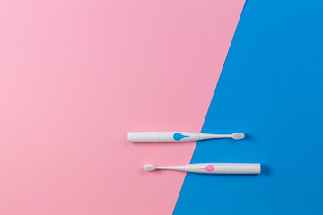 Two electric toothbrushes on blue and pink background. Top view