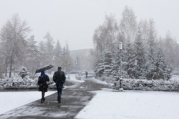 Fototapeta na wymiar snowy city street, park and people with umbrellas
