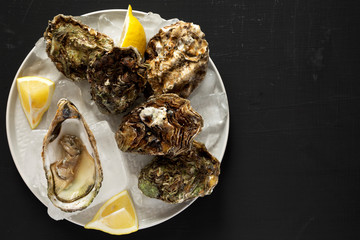 Fresh oysters on a plate over black background, overhead view. From above, flat lay, top view. Copy space.