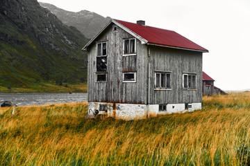 Fototapeta na wymiar Old damaged wooden norwegian house with a red corrugated iron rooftop in the village Vinstad on Lofoten Islands in Norway.