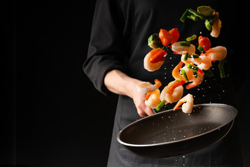 Seafood, Professional cook prepares shrimps with vegetables. Frost in the air, Cooking seafood, healthy vegetarian food and food on a dark background. Horizontal view. Eastern kitchen, banner