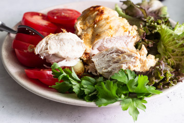 Baking chicken breast (fillet) with cream cheese sauce on a plate with green salad, tomatoes and grilled zucchini.