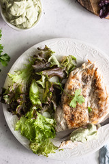 Grilled chicken steak with sauce on a white plate served with green salad.