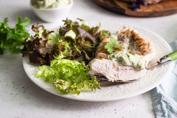 Grilled chicken steak with sauce on a white plate served with green salad.