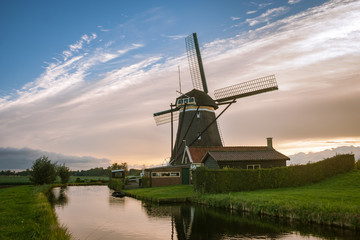 Classic scene of a dutch windmill and house near a canal with a great sky as background.
