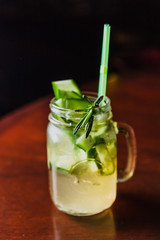 Refreshing summer lemonade with cucumber and rosemary in a glass jar at the bar with lights in the background