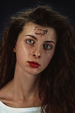 Portrait of young woman with mental health problems. The image with the tattoo on the forehead with the words I am ugly-beautiful. Concept of hidding the true feelings, psycological trouble, treatment