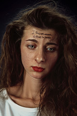 Portrait of young woman with mental health problems. Tattoo on the forehead with the words I trust no one-believe in people. Concept of hidding the true feelings, psycological trouble, treatment.