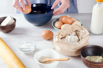 Woman cracking an egg into the blue bowl, baking cake process.Base ingredients for baking on the kitchen table