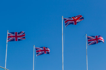 Four Union Jack, British flags on poles flying in the wind.