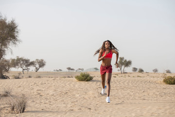 Strong African Black woman with long braids in hair in the desert wearing red sportswear runs toward the camera   