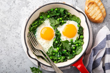 Healthy breakfast. fried eggs with kale, spinach and green peas in red skillet