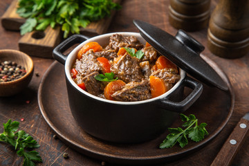 beef stew with vegetables in black pot on dark wooden background,