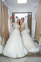 Fototapeta na wymiar Friends in wedding dresses making selfie in salon