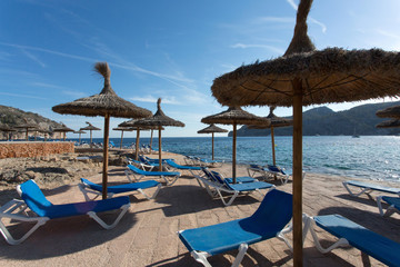 Deckchairs and thatched umbrellas in sunny Mediterranean Island Resort with crystal clear water and blue sky.