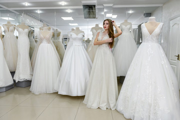 Fototapeta na wymiar Elegant cheerful lady in bridal dress standing in wedding salon