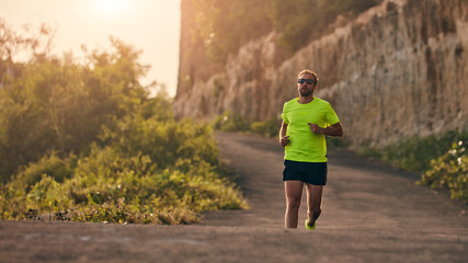Obraz premium Mężczyzna jogging na zjazd / pod górę na przedmieściach górskiej drodze.