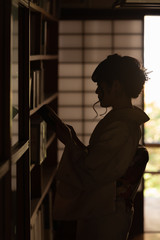 A japanese kimono girl is reading a book in front of the bookshelf at the ancient temple. Kyoto, Japan