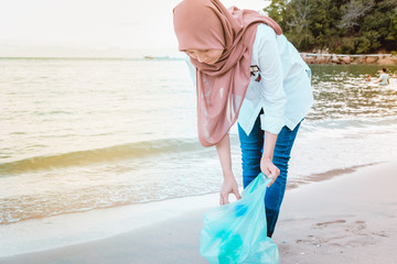 Young female environmental activist picking up trash like plastic bottle while holding biodegradable garbage bag by the beach.