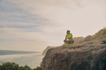 Sportsman making pause after workout on a tropical cliff.