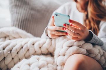 woman sitting on couch with wool blanket and smartphone